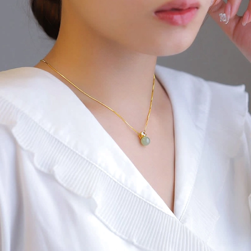 Close-up detail of jade pendant necklace worn on neck, showing slim 925 sterling silver gold-plated chain against white blouse