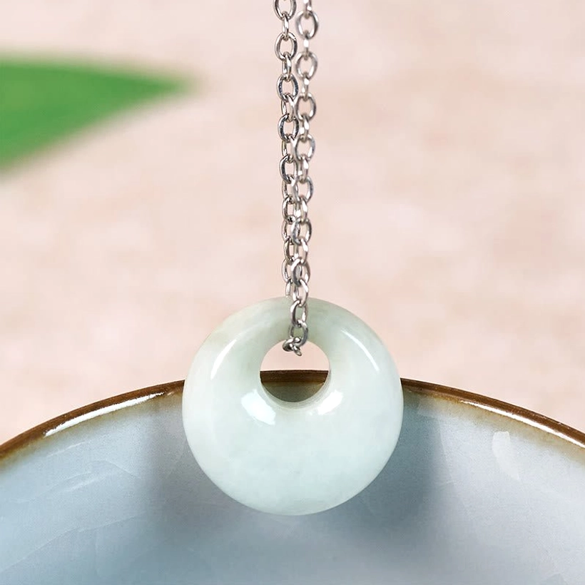 Natural jade round pendant on silver twisted chain resting on ceramic bowl, handmade jewelry