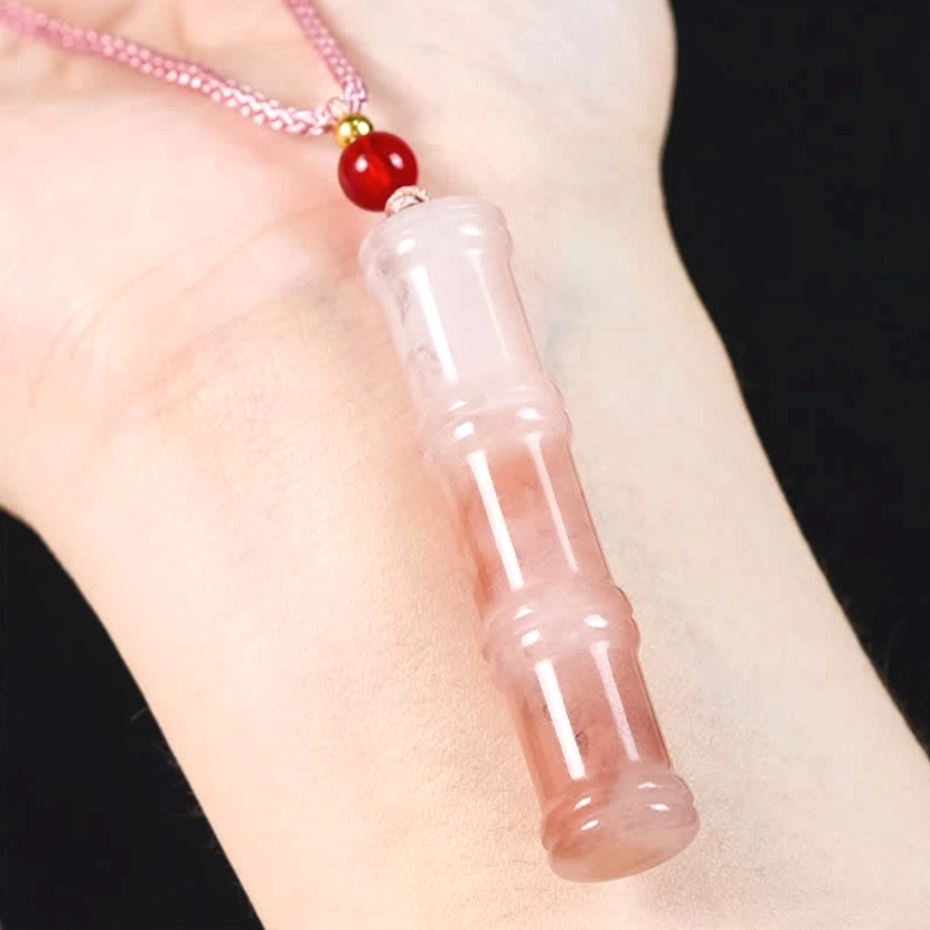 Pink quartzite jade bamboo pendant necklace worn on wrist in flat lay context, showing red accent bead, braided cord, and practical jewelry wear styling