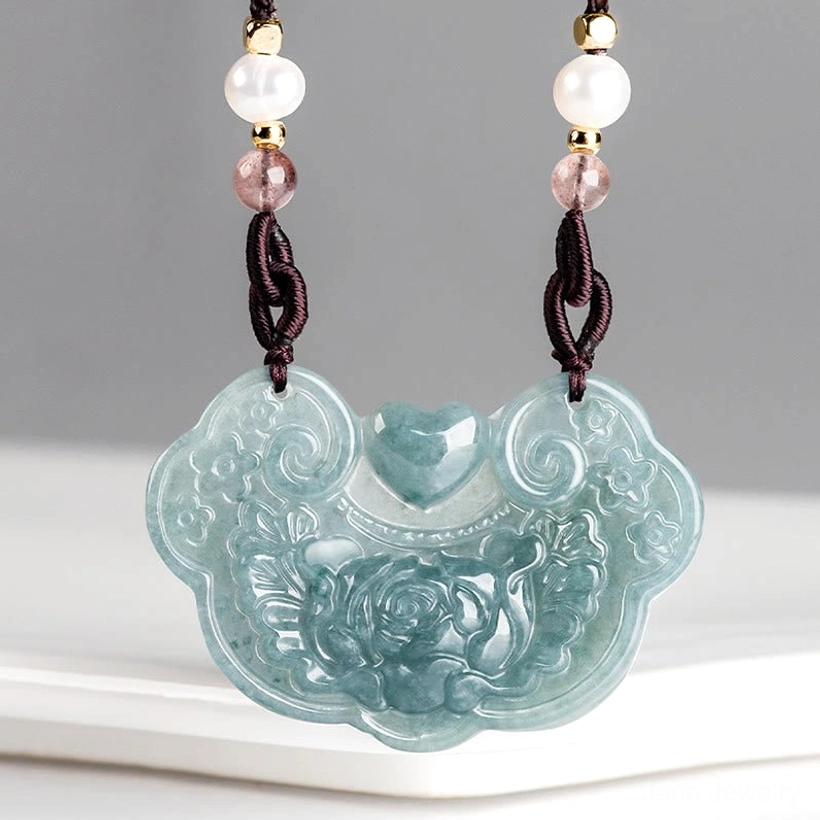 Overhead view jade peony lock pendant on white ceramic tray displaying full front carved floral patterns, clear bluish jade texture detail
