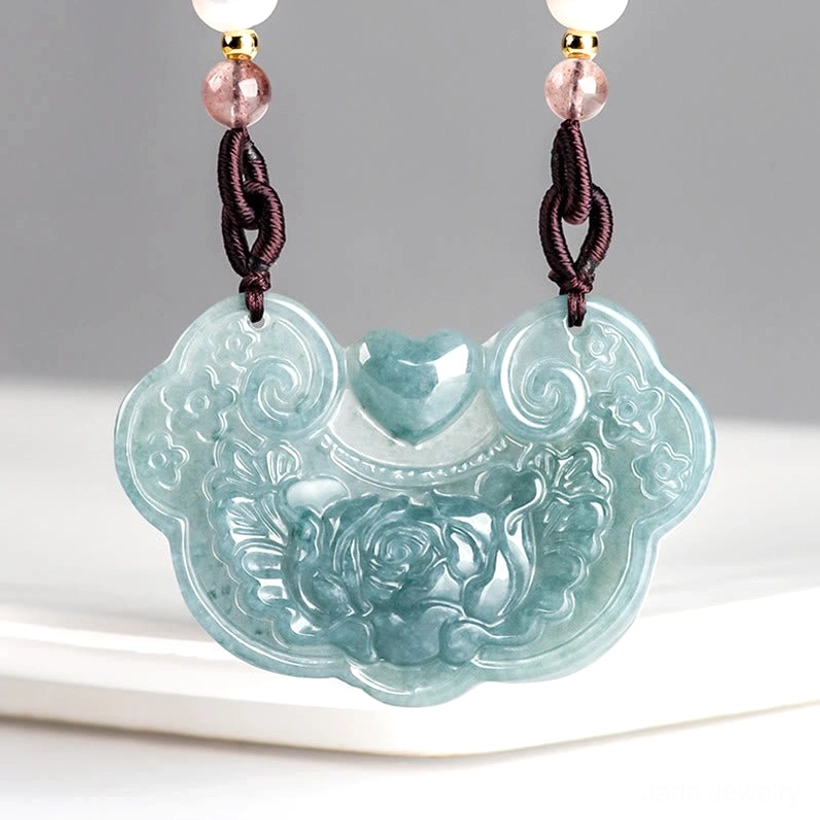 Natural jade peony ruyi lock pendant necklace carved with floral motifs, front view displayed on white ceramic platform, bluish jade prosperity pendant