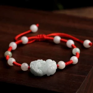 Close-up top-down view of jade Pi Xiu bracelet displaying intricately carved wealth guardian, mixed jade beads, and tidy red woven rope structure