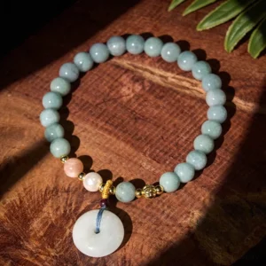 Handmade jade beaded bracelet with peace buckle pendant displayed on wooden board with green leaf styling