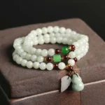 Natural jade pixiu abundance bracelet with multi-strand design featuring light green jade beads and red-brown decorative accents on wooden box