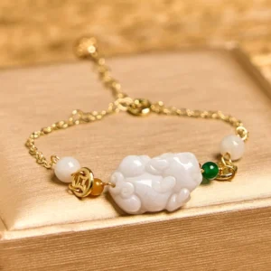 Close-up detail of jade Pixiu bracelet showing light gold adjustable chain, white Pixiu carving, and decorative beads on satin fabric