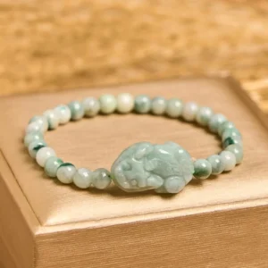 Natural green jade Pixiu lucky bracelet displayed overhead on golden jewelry tray showing mixed light green and white jade beads with hand-carved Pixiu charm