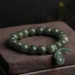 Dark green jade Pi Xiu prosperity bracelet with carved pendant and bead tassel, close-up top view on wooden block