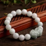 Pale white jade round beads with light green carved Pixiu charm on wooden lattice display tray, overhead view