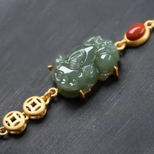 Close-up detail of carved jade pixiu charm on gold-toned chain bracelet with red agate accents