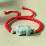 Natural jade Pixiu protection bracelet with red cord overhead flat lay view showing carved jade Pixiu pendant and braided string