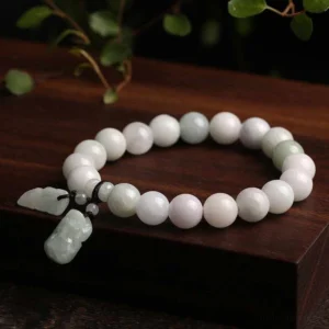 Jade pixiu wealth bracelet side view on wooden display block with green foliage and natural lighting