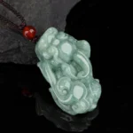 Natural jade Pixiu wealth necklace pendant with brown cord and red agate bead, overhead view on dark slate background