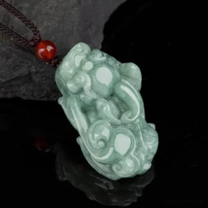 Natural jade Pixiu wealth necklace pendant with brown cord and red agate bead, overhead view on dark slate background