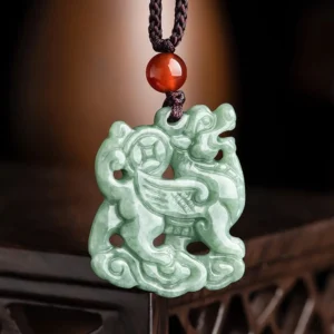 Light green carved jade Pixiu pendant with cloud base and red agate bead on black cord - front close-up view