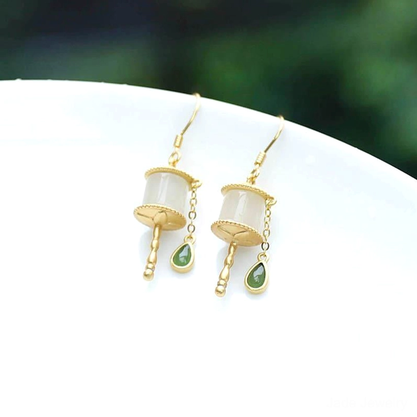 Jade prayer wheel drop earrings on white ceramic plate with green background, featuring gold metal parts, milky white jade tube, and green teardrop charms