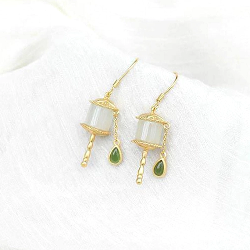 Sterling silver jade prayer wheel drop earrings on white linen cloth, displaying gold metal trim, milky white jade cylinder, and green teardrop pendants with soft texture