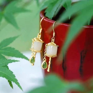 Side view of jade prayer wheel drop earrings showing gold-toned metal trim, white jade cylinder, and green teardrop pendant charm
