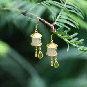 925 sterling silver jade prayer wheel drop earrings with milky white jade tube and green teardrop charm, displayed on pine branch with foliage background