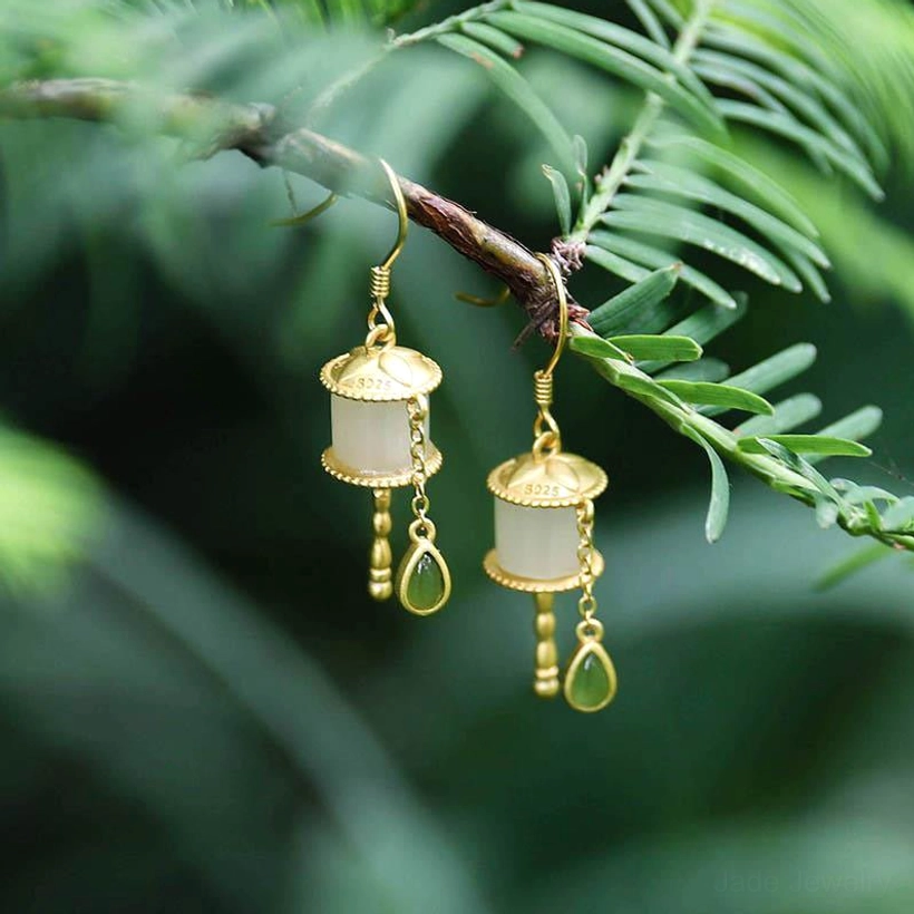 925 sterling silver jade prayer wheel drop earrings with milky white jade tube and green teardrop charm, displayed on pine branch with foliage background