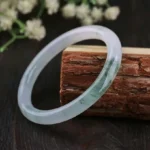 Natural jade bangle bracelet with pale translucent base and green cloud patterns, three-quarter view