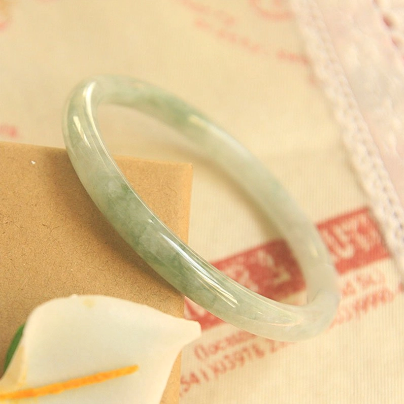 Pale green natural jade bangle bracelet slim circular design photographed from low side angle with artificial flowers
