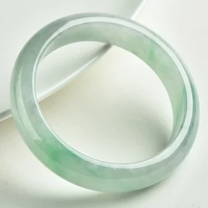 Authentic green jade bangle bracelet photographed at three-quarter angle on white background, showcasing rounded solid jade design and glossy polished texture