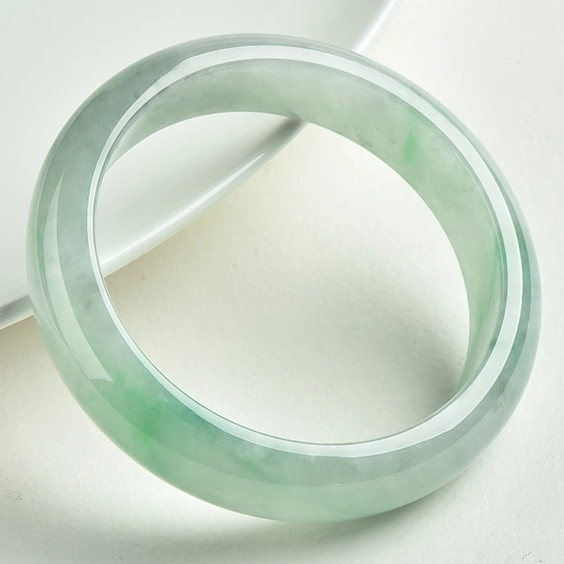 Authentic green jade bangle bracelet photographed at three-quarter angle on white background, showcasing rounded solid jade design and glossy polished texture