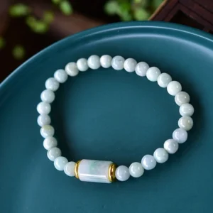 Natural jade prosperity bracelet top-down flat lay view showing pale green round jade beads with gold-toned center barrel bead on ceramic tray background