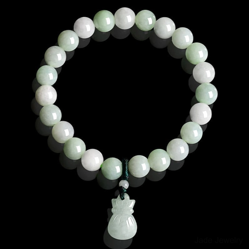 Top-down flat lay view of circular jade beaded bracelet with carved money bag pendant on black background, highlighting light green jade stones