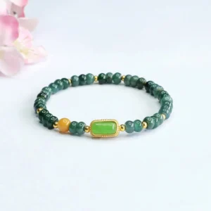 Natural green jade prosperity bracelet flat lay with gold-trimmed centerpiece and topaz accents on pink floral desktop