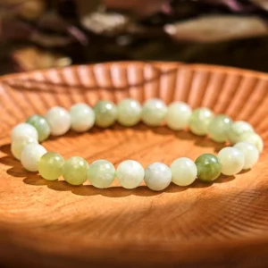 Natural jade prosperity bracelet with gradient green beads displayed on wooden plate, handmade jade stone bracelet for wealth and abundance