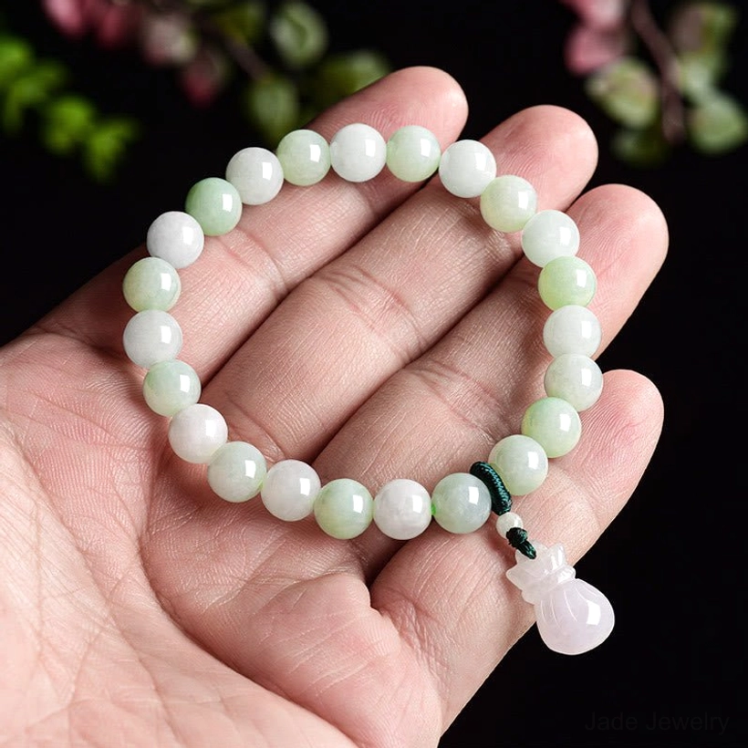 Jade bead bracelet held in palm first-person view, gradient light green beads with pale pink jade money bag pendant visible in hand