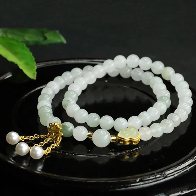 Uniform Tianshan jade beads bracelet with elegant gold lotus charm and pearl tassel pendant, flat lay on dark circular tray