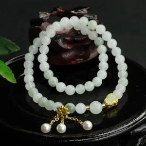 Double-circle jade beaded bracelet with pale green Tianshan jade beads, gold clasp, and pearl tassel detail on black decorative tray