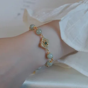 Natural jade bracelet overhead view on white cloth backdrop, showing decorative square charm with central green gemstone