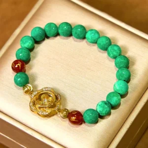 Jade mantra bracelet with spinning flower charm on beige jewelry presentation box, featuring matte green jade beads and gold rose charm with crystals