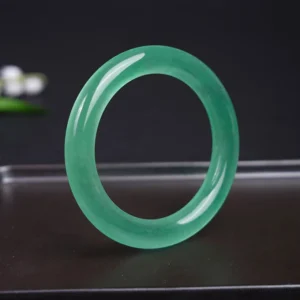 Authentic jade bangle bracelet displayed from top oblique angle on decorative metal tray, showcasing even jade coloring and glossy finish
