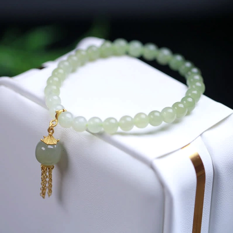 Hetian jade charm bracelet side view on white jewelry box, smooth round jade beads with sterling silver tassel accent pendant