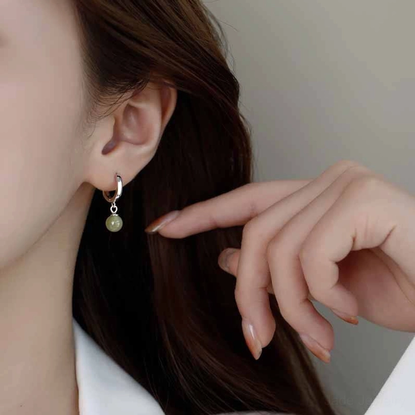 Light green jade bead earring worn on earlobe with hand gesture and manicure, side wearing view indoor lighting