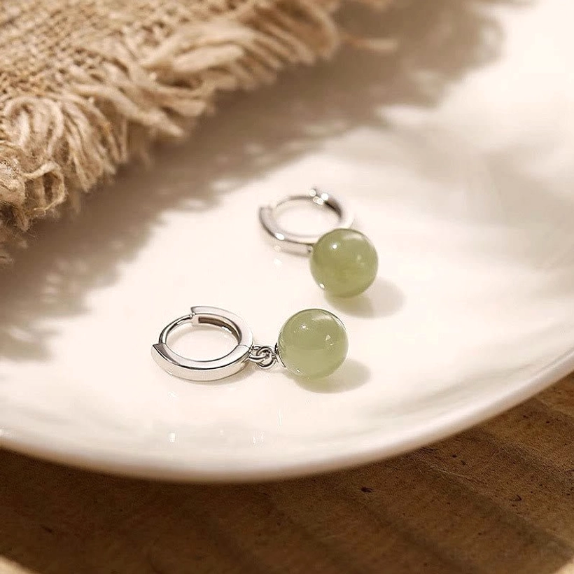 Pair of light green jade bead prosperity earrings displayed on ceramic plate and burlap fabric, flat lay styling