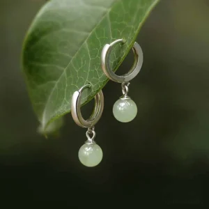 Light green jade bead drop hoop earrings in 925 sterling silver, top-down close-up view on natural green leaf background