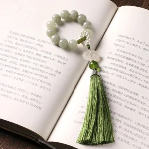 Handmade jade beaded mala bracelet with matching green tassel and pink stone pendant resting on open book pages