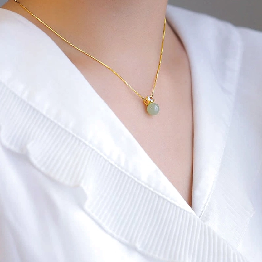 Front neck detail of light green jade prosperity pendant necklace with minimalist delicate gold chain and clear gemstone accent
