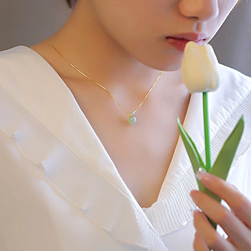 Woman wearing light green jade prosperity pendant necklace with white blouse, soft fresh styling with natural light