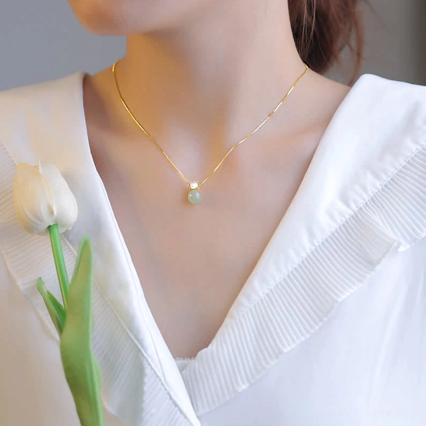 Woman wearing light green jade prosperity pendant necklace with gold chain on collarbone, styled with white ruffled blouse