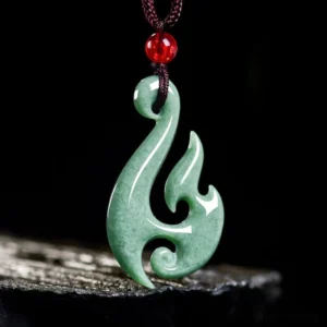 Jade flame pendant necklace on textured surface with dark cord and red accent bead, prosperity jewelry detail
