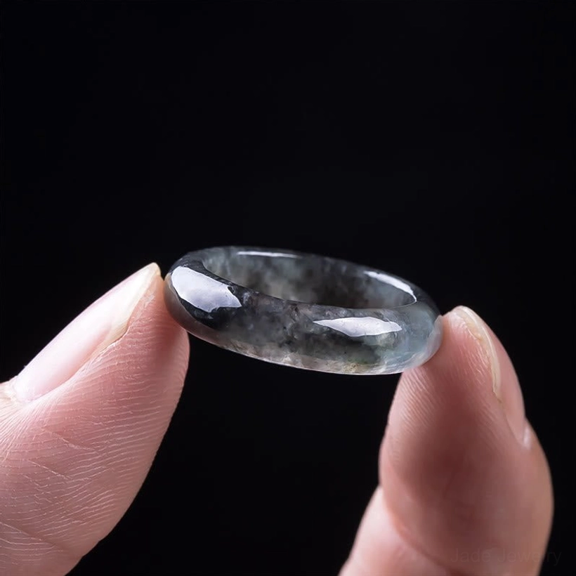 Close-up detail of polished natural jade prosperity ring held between fingers, showing texture and reflective surface