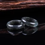 Pair of handcrafted natural jade prosperity rings displayed on reflective black surface, showing polished dark jade bands with mirrored reflections