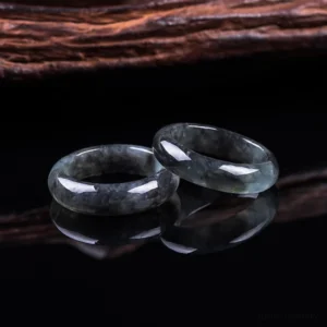 Pair of handcrafted natural jade prosperity rings displayed on reflective black surface, showing polished dark jade bands with mirrored reflections