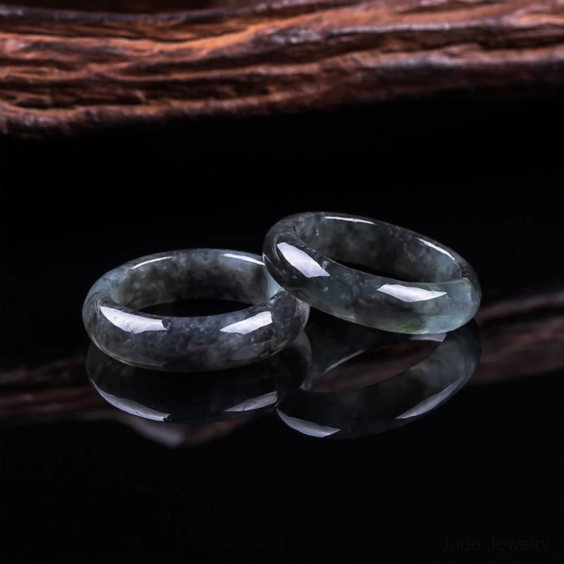 Pair of handcrafted natural jade prosperity rings displayed on reflective black surface, showing polished dark jade bands with mirrored reflections